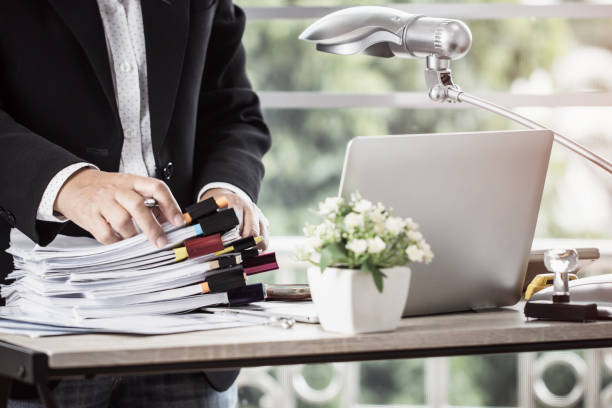istock Accounting planning budget concept : Business woman offices working for arranging documents unfinished stack of document papers with pen, clip papers on busy office desk 1064568672