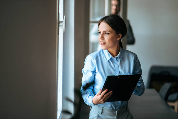 istock Young businesswoman with clipboard looking through window. 1064568702