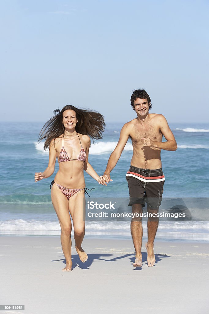 Jovem casal correndo na praia vestindo trajes de banho - Foto de stock de 30 Anos royalty-free