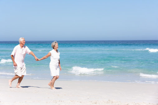 Senior Couple On Holiday Running Along Sandy Beach holding hands