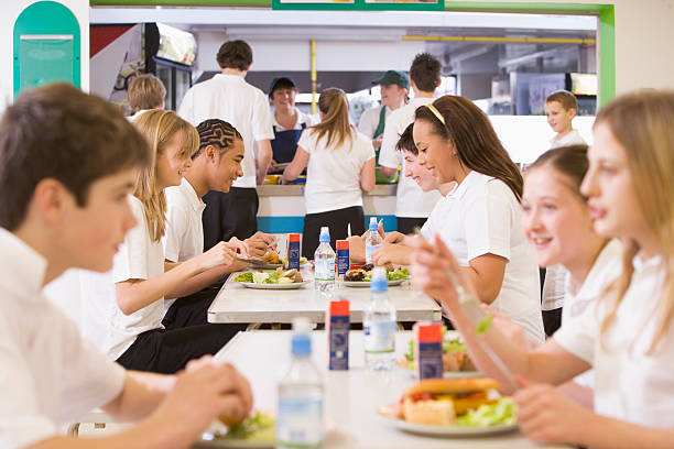Happy Latin American schoolgirl eating her school lunch at the cafeteria with a group of friends and looking at the camera smiling