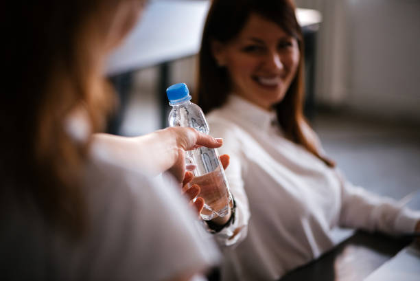bela jovem estudante feminino dando a garrafa de água para sua amiga. - water divide - fotografias e filmes do acervo