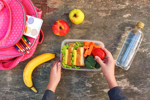 Sandwiches, fruits and vegetables in food box, backpack on old wooden background. Concept of child eating at school. Top view. Flat lay.