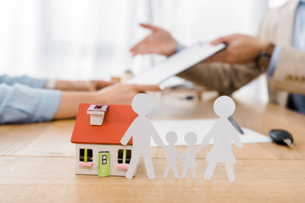 White paper cut family and house model on wooden table with blurred people at background, life and house insurance stock photo