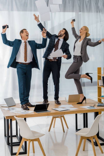 istock joyful insurance workers dancing on table and throwing papers at meeting in office 1064577348