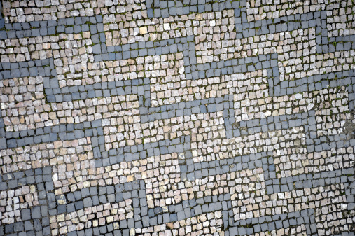 Black and white cobble stones, arranged in a zigzag pattern, line a medieval European street.