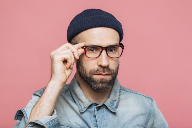 istock Handsome bearded man with serious expression wears spectacles and glasses, dressed in denim fashionable shirt, isolated over pink background. People, facial expressions and emotions concept. 1064585926