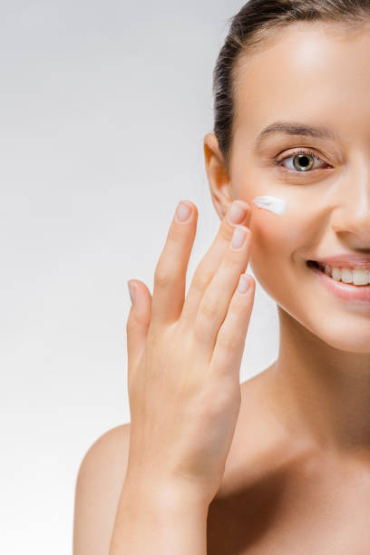istock young beautiful woman applying white cream on cheek 1064586430