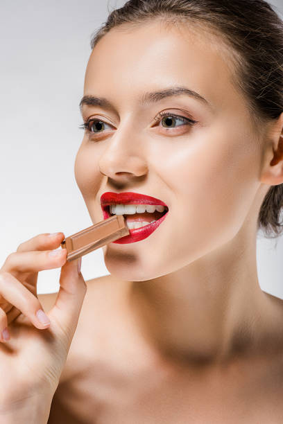 istock young beautiful woman with red lips biting chocolate piece 1064587698