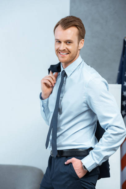 istock joyful young businessman with jacket over shoulder looking at camera in office 1064592276