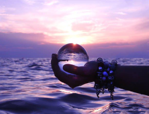 Hands of woman holding crystall ball at sea sunset stock photo