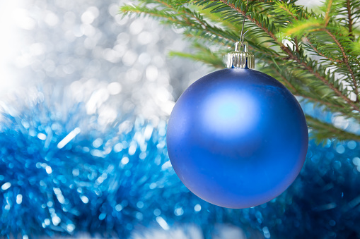 Christmas decorations, one blue ball hanging on Christmas tree on a background of tinsel foil