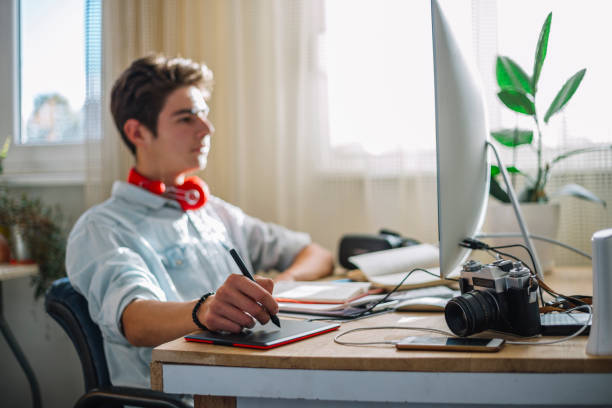 Young teenage boy  - graphic designer at work Young teenager from home doing their work or exercise for the exam, deals with graphic design and works in the program Photoshop. broadcast programming photos stock pictures, royalty-free photos & images