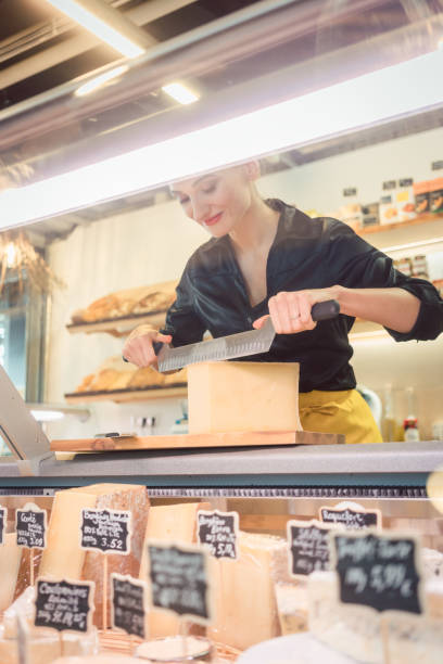 istock Young shop clerk in deli cutting cheese 1064642278