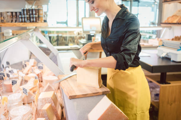 istock Young shop clerk in deli cutting cheese 1064642330