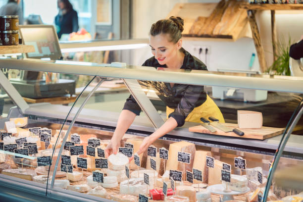 mujer de vendedor de tienda clasificación queso en la exhibición del supermercado - delicatessen fotografías e imágenes de stock