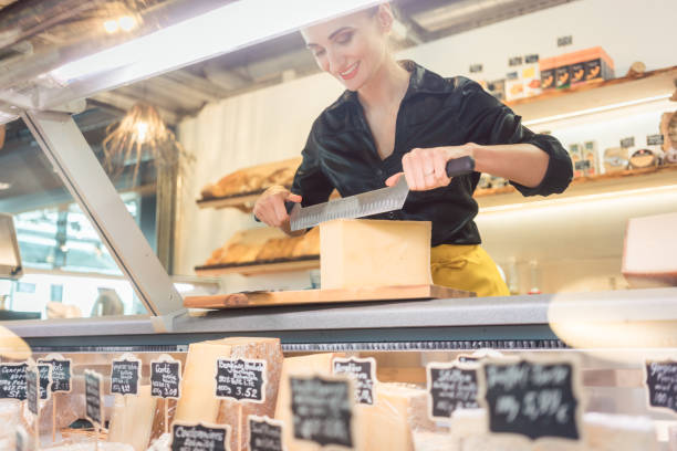 istock Young shop clerk in deli cutting cheese 1064642568