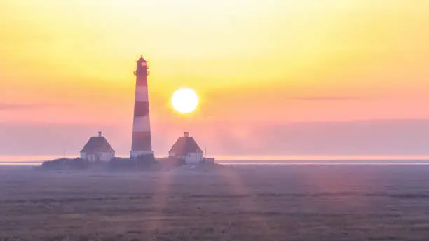 The image shows the famous lighthouse of Westerhever at the north sea during a winter sunset