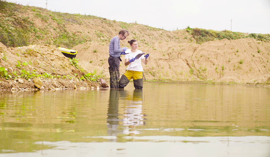 Two environmental scientists standing in the water. A woman checking with the GPS navigator and marking point of research on the map.
