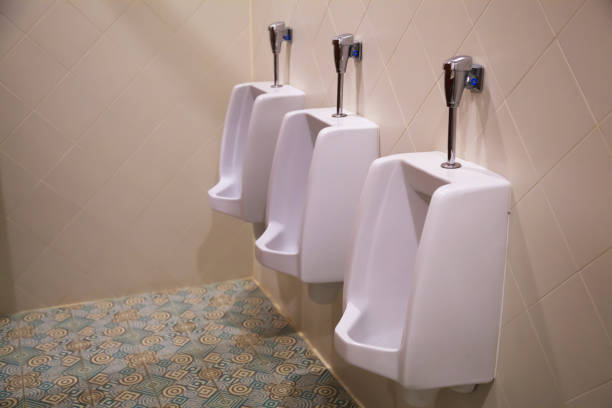 clean white male lavatory urinal sanitary ware vessel fixture or fitting attached upright to a wall used by men for urinating or excreting urine in restroom, water closet. home interior design concept - urinal clean contemporary in a row imagens e fotografias de stock