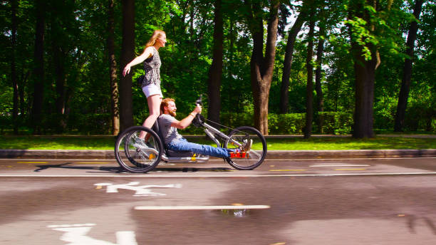 Young couple enjoying time outdoors. She is cycling, he is sitting in a wheelchair.