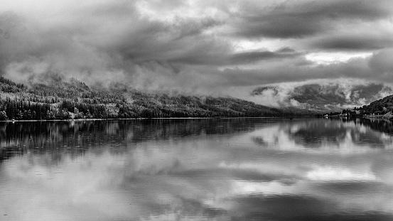 Beautiful reflection in the Tyrifjorden (Lake Tyri) after a rainy day in Norway. Dramatic sky, fog, trees and mountains are perfectly mirrored in the lake.