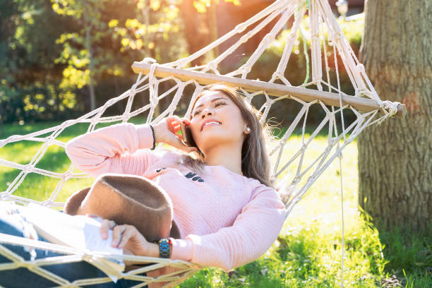 istock Young woman talking on mobile phone and lying down on a hammock 1064686772