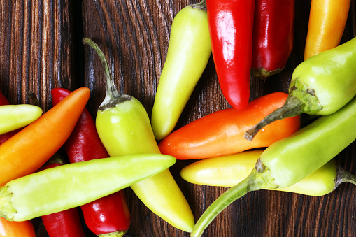 Stock photo showing close-up view of white background with a small heap of red, orange and yellow mini peppers (Capsicum annuum), with green stems.