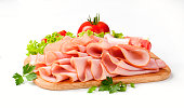 Thinly sliced ham and veggies atop a wooden cutting board