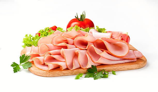 Thinly sliced ham and veggies atop a wooden cutting board stock photo