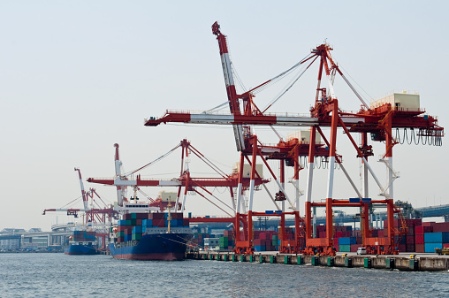 Gantry cranes loading/unloading containers at a container yard in Yokohama, Japan. Container ships are moored at the port.