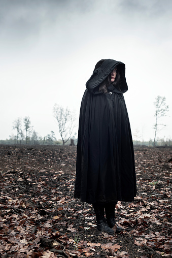 Woman in black cape in moody landscape.