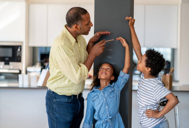 heureux père mesure ses enfants à la maison - instrument de mesure photos et images de collection