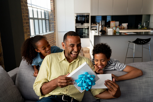 Happy African American kids surprising their father with a gift at home and smiling - Father's Day concepts