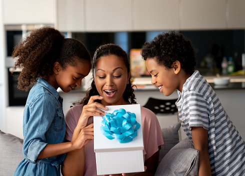 Happy African American kids surprising their mother with a gift at home and smiling - Mother's Day concepts