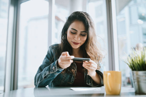 hermosa joven depositar cheque con smartphone - banca electrónica fotografías e imágenes de stock