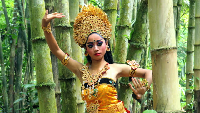 Young Balinese dancer performing Legong dance in a bamboo forest