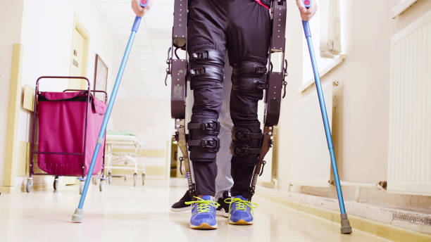 Legs of invalid in robotic exoskeleton walking through the corridor Legs of disable man in the robotic exoskeleton walking through the corridor of the rehabilitation clinic. Doctor helping him. powered exoskeleton photos stock pictures, royalty-free photos & images