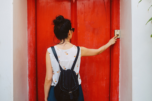Young woman visiting her friend in Bangkok, Thailand, ringing the doorbell.