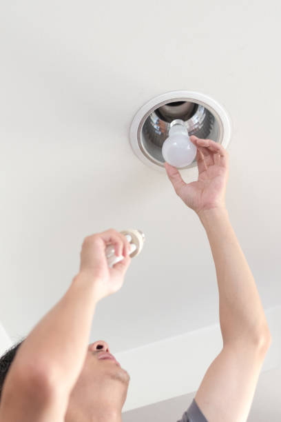 istock Power saving concept. Asia man changing compact-fluorescent (CFL) bulbs with new LED light bulb. 1064814060