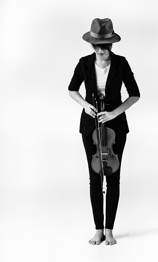 The lady is wearing black suit and hat,holding violin and bow in hand,standing on background,prepare for playing ,vintage and art tone