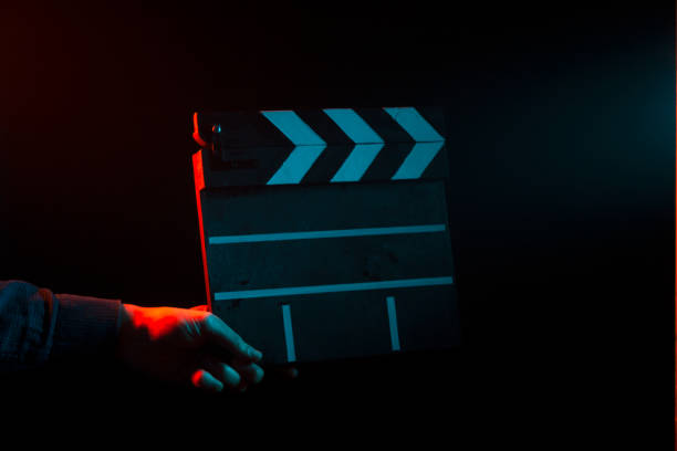 バックライトを赤と青と黒の孤立した背景に撮影の前に、手で映画館のカチンコを閉鎖 - projectionist ストックフォトと画像