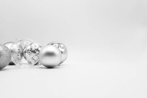 This image shows a close-up defocused abstract view of silver color glittering balls, baubles and fabric ribbon holiday decorations on a sparkling green background with bokeh.