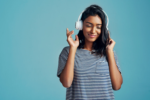 Cropped shot of a beautiful young woman wearing headphones against a blue background