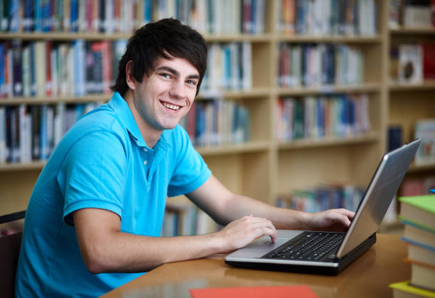 istock Male student working on laptop in library turns and smiles 1064875804
