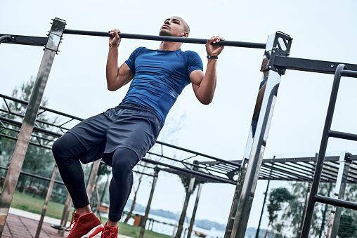 An african man is exercising at open air gym. Close-up photo of black african handsome guy in sports clothes is doing exercises for his hands