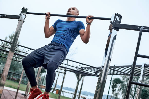 An african man is pulling up at open air gym An african man is exercising at open air gym. Close-up photo of black african handsome guy in sports clothes is doing exercises for his hands chin ups stock pictures, royalty-free photos & images