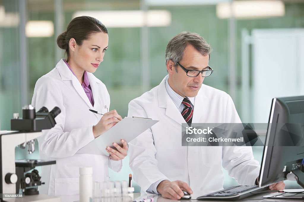 Dos personas realizar trabajos de investigación en la computadora en los análisis de laboratorio - Foto de stock de 25-29 años libre de derechos