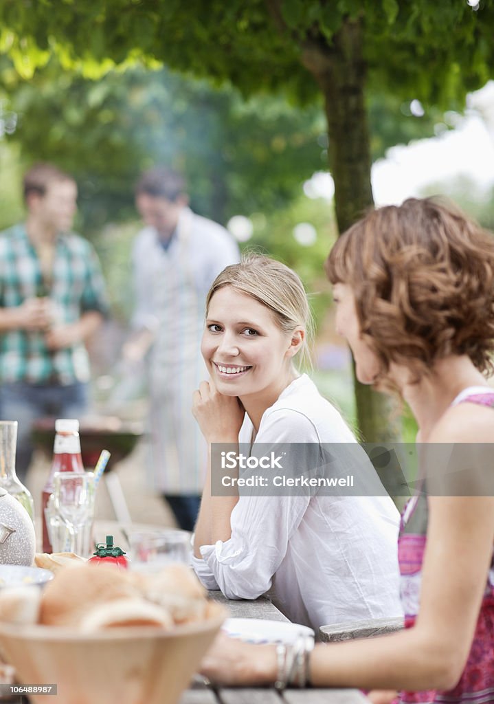 Young couple sitting by picnic table with people in the background  25-29 Years Stock Photo