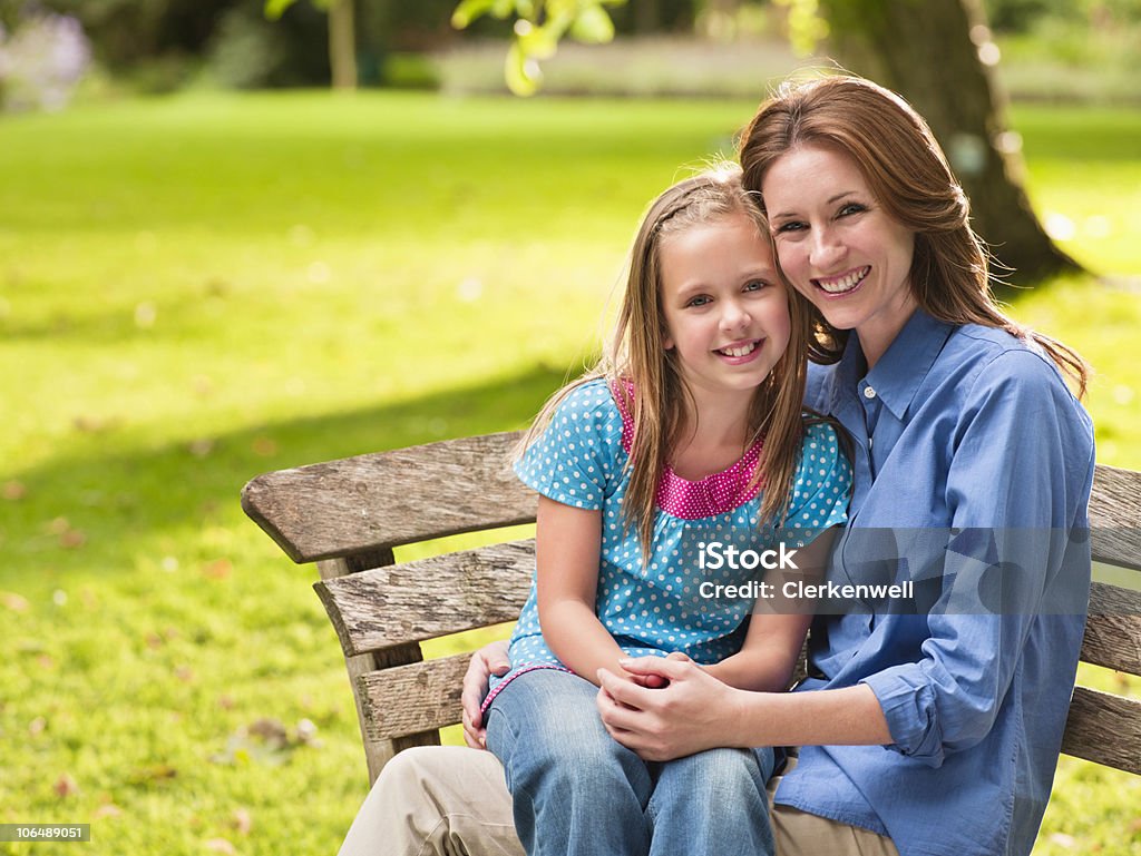 Sorridente madre con figlia (8-9) seduto sulla panchina nel parco - Foto stock royalty-free di 35-39 anni